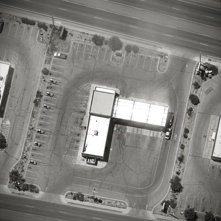 Monochrome overhead surveillance frame of a drive-through car wash, its queueing lane and parking apron
